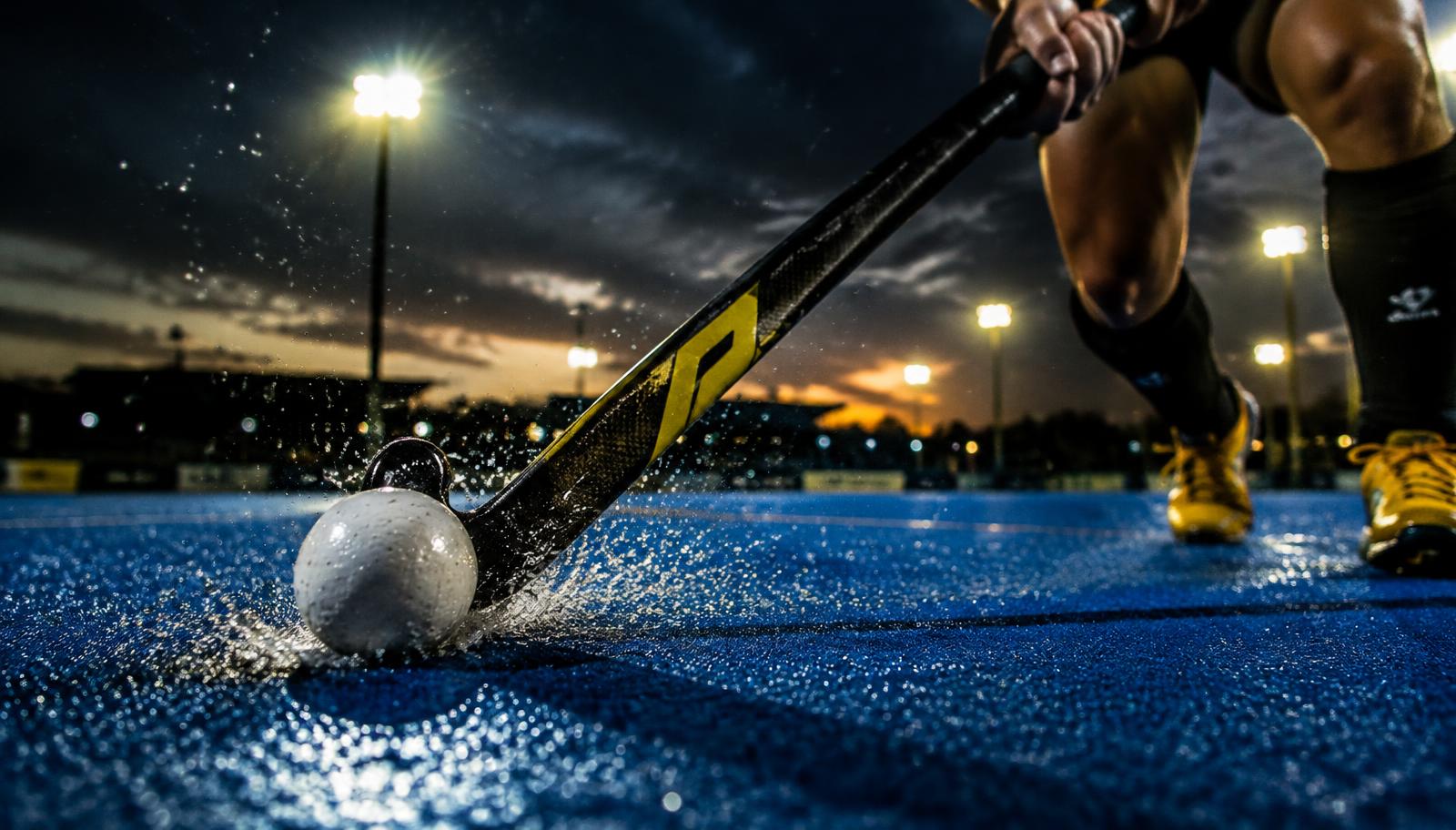 Hockeystick raakt de bal op een nat kunstgrasveld